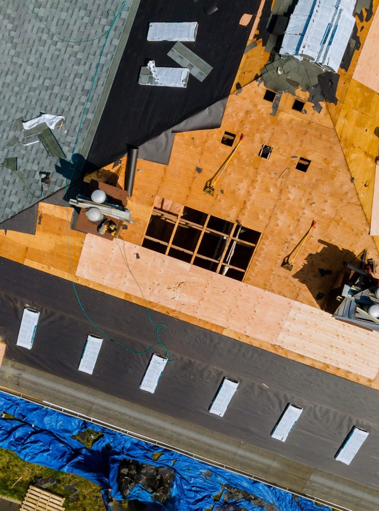 A roofer nailing shingles with air gun, replacing roof cover protection being applied, apartment development