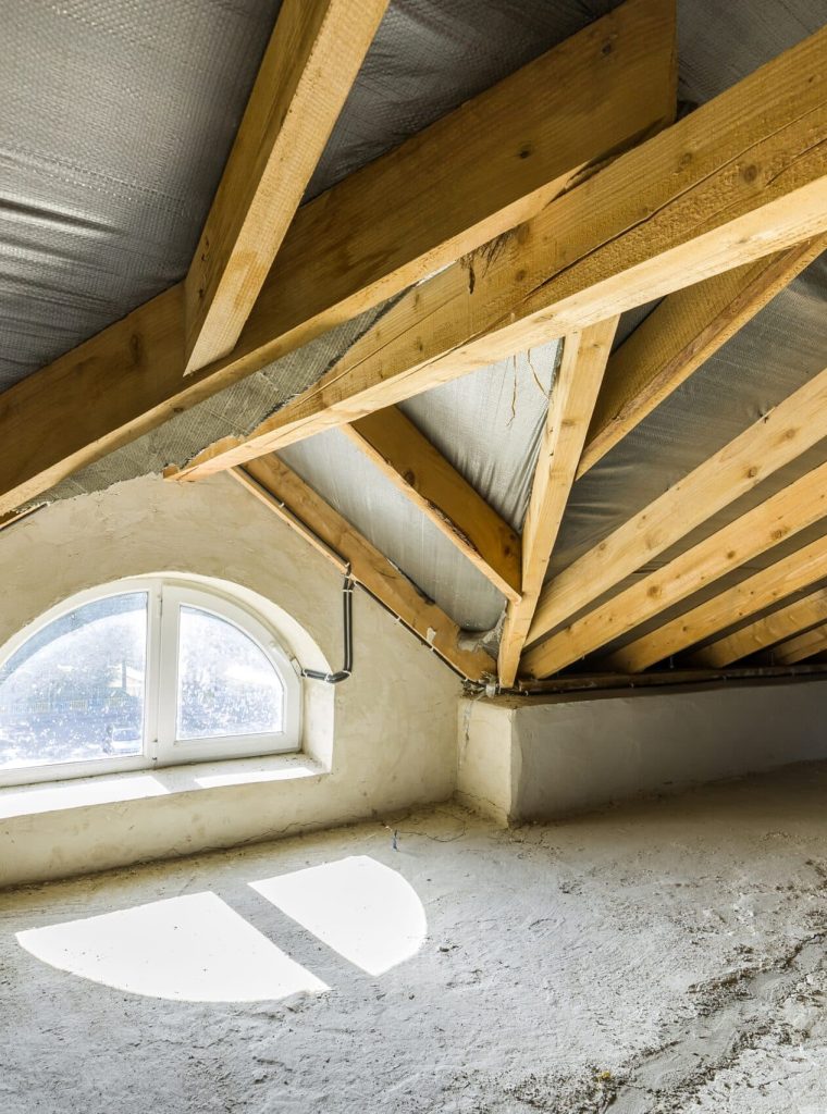 Attic of a building with wooden beams of a roof structure and a small window.