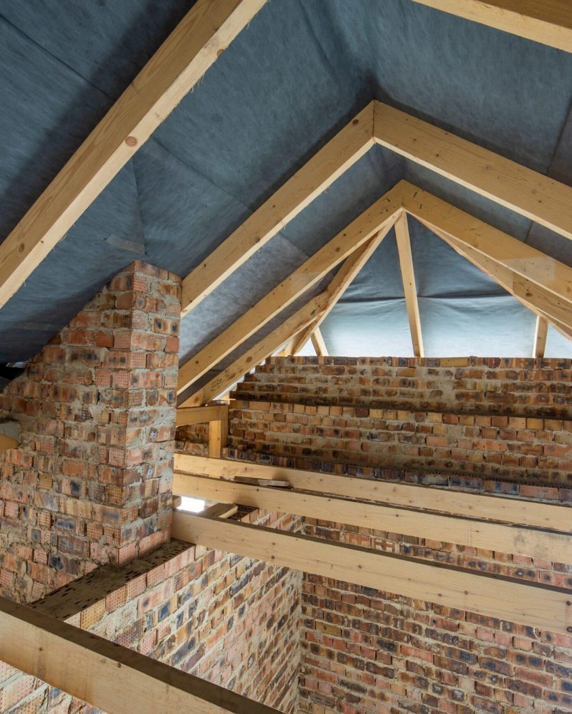 Attic space of a building under construction with wooden beams of a roof structure and brick walls. Real estate development concept.